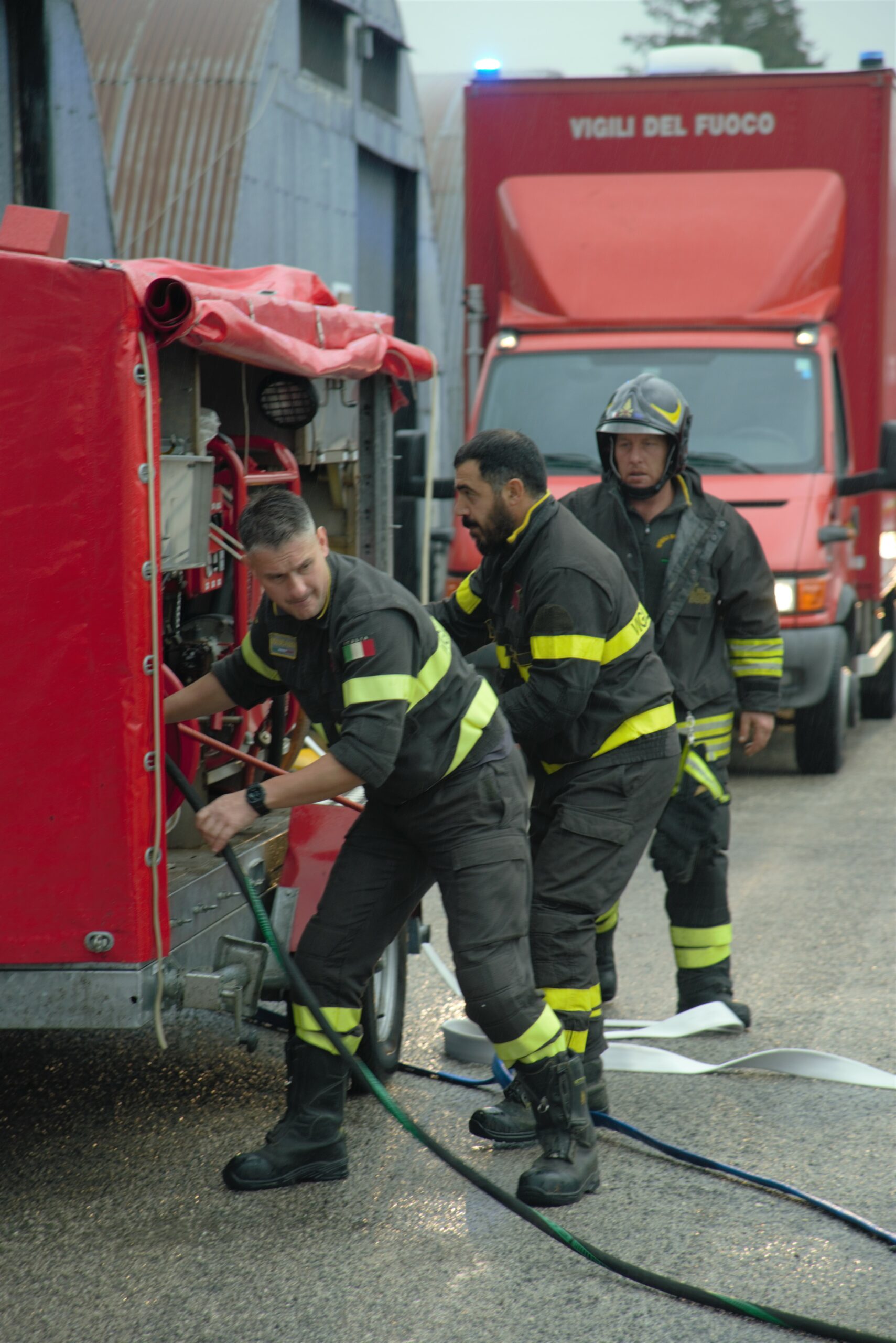 Three firefighters (men) in a special uniform standing next to equipment and are preparing nozzles.