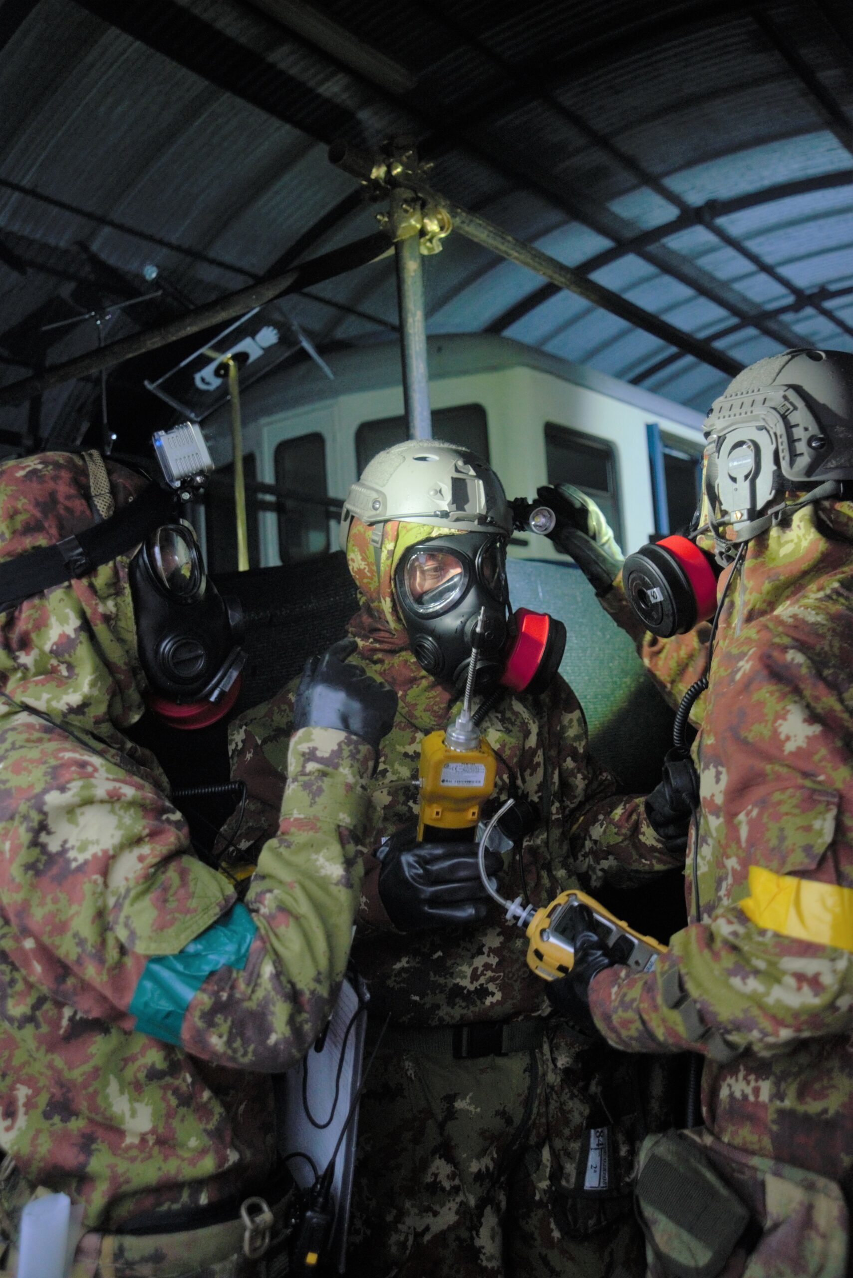 Three Military staff in a uniform wearing a respirator. Two of them are checking the respirator of the man in the middle.