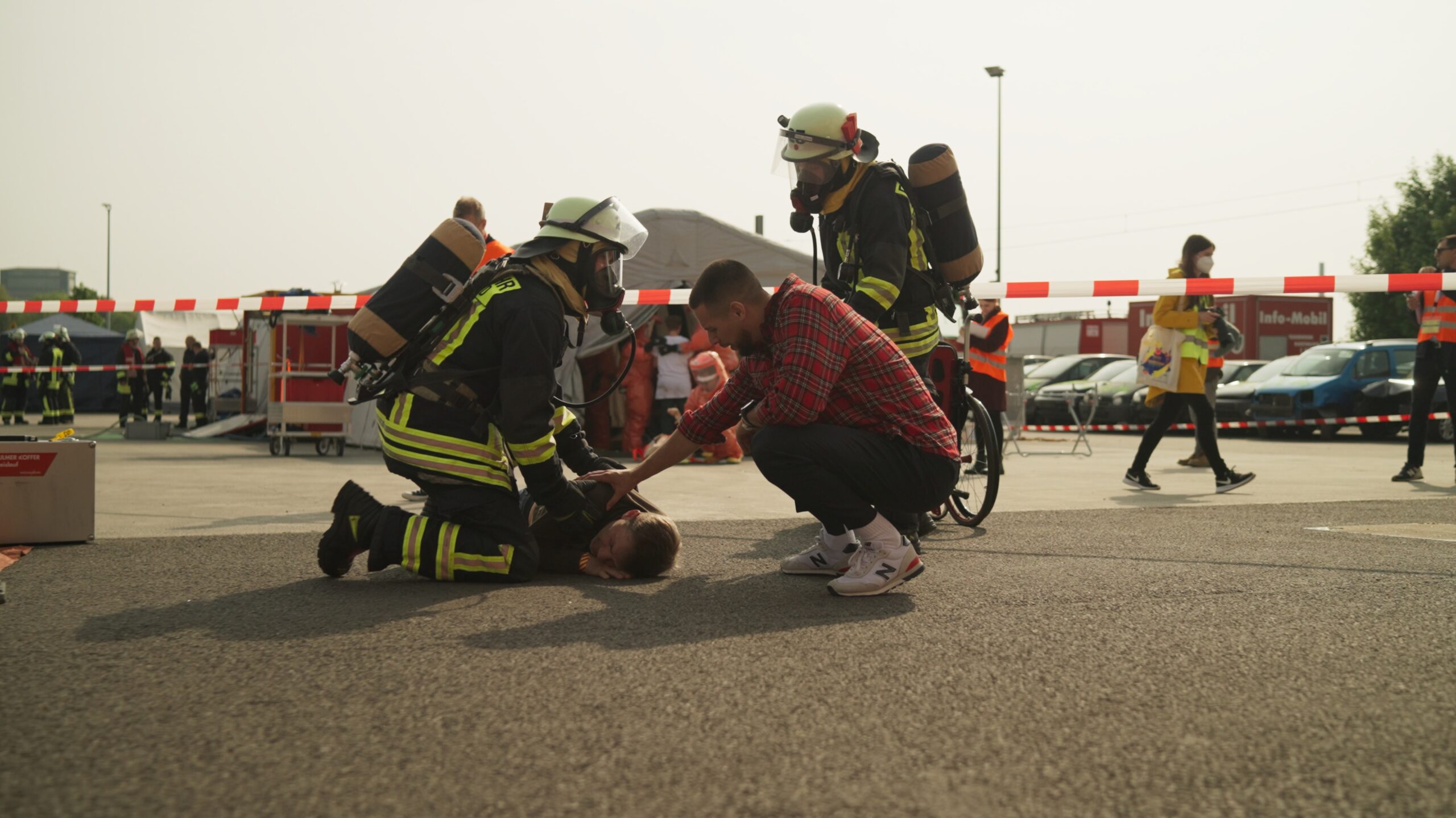 Two firefighters checking the health condition of participant lying on the ground and another participant putting his hand on shoulders of lying participant
