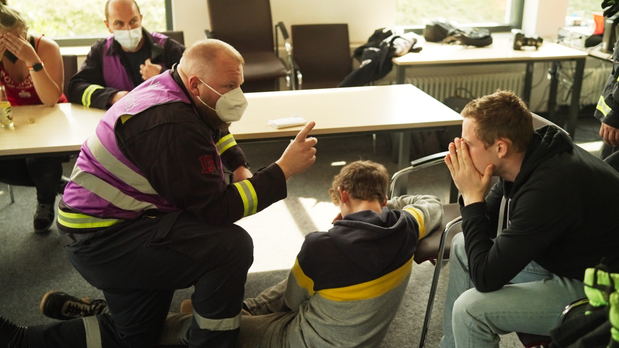 A responder is warning and explaining something to two participants in the room. Another participant and responder are sitting on the chair behind