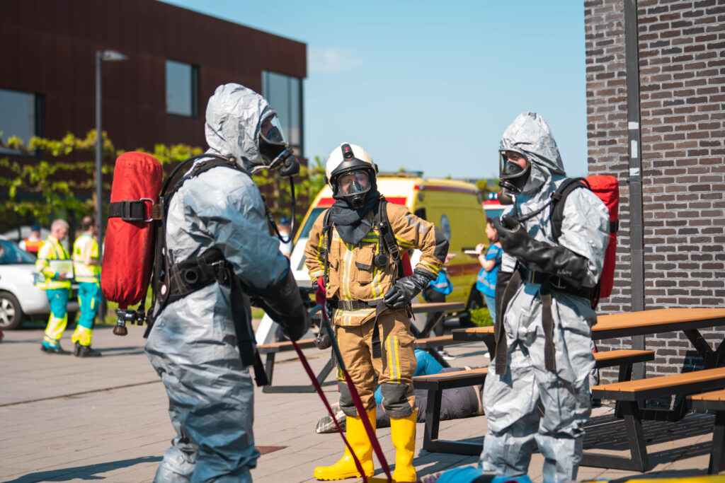 Three people in the front are in uniform, two of them are in grey hazmat suits.
