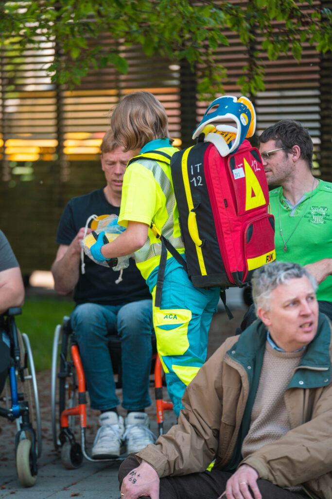 Five people in the photo. Four people are in the wheelchair. A person in the green uniform is giving something to the man in the middle of the photo.